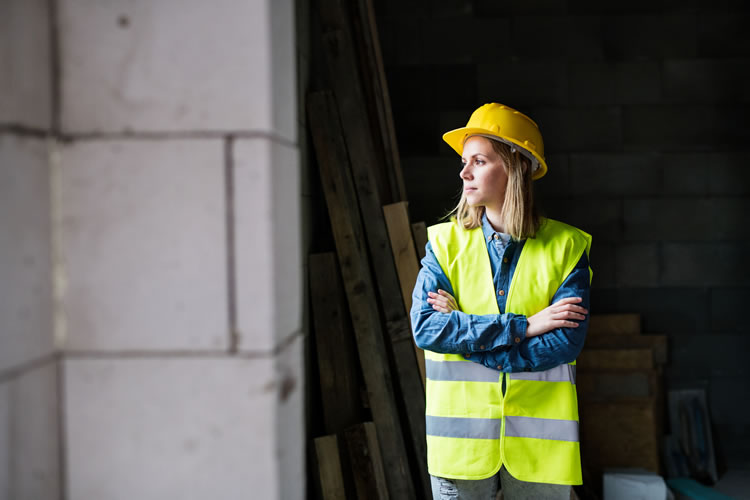 A woman wearing a hard hat and hi-viz jacket standing in an unfinished building